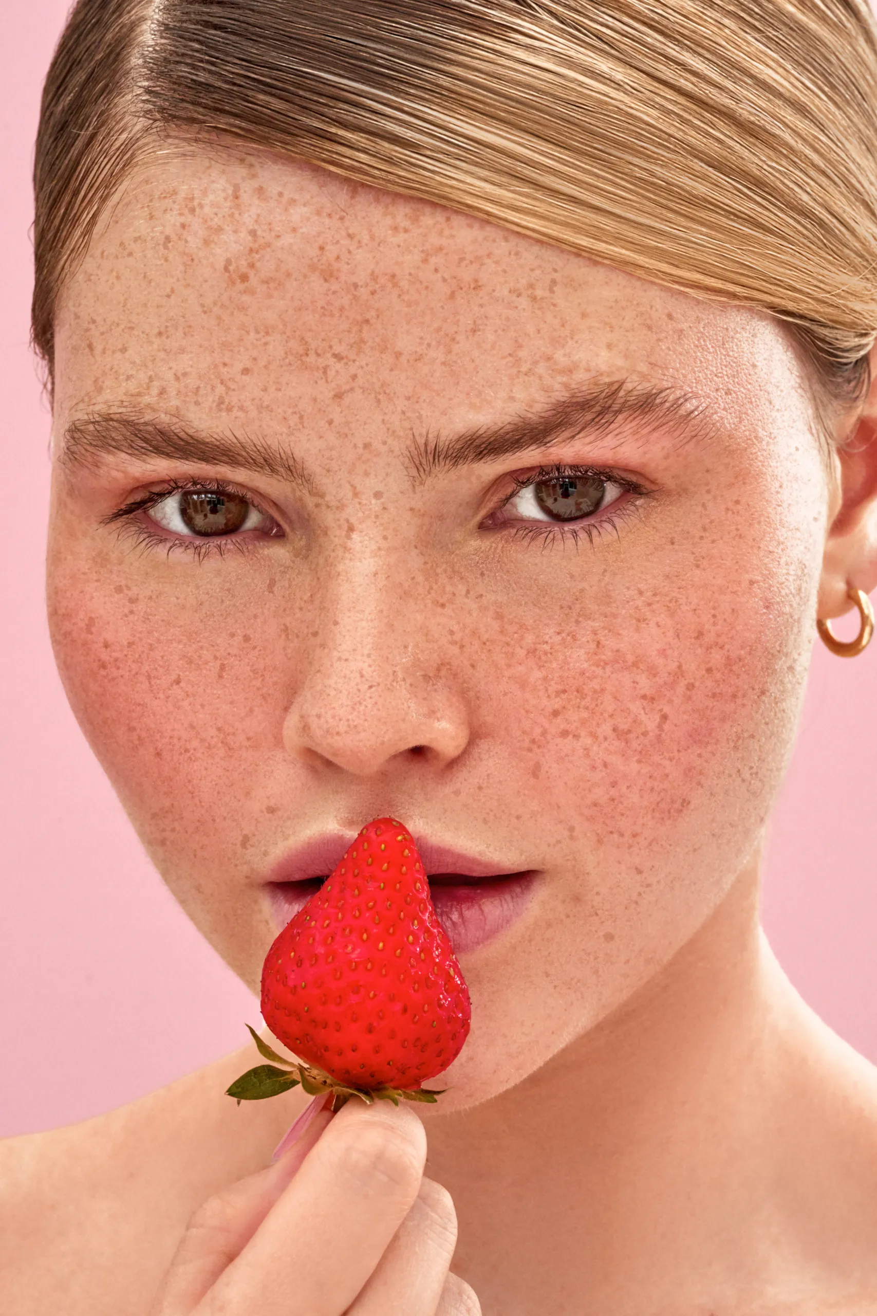 A woman holding a strawberry in her mouth.