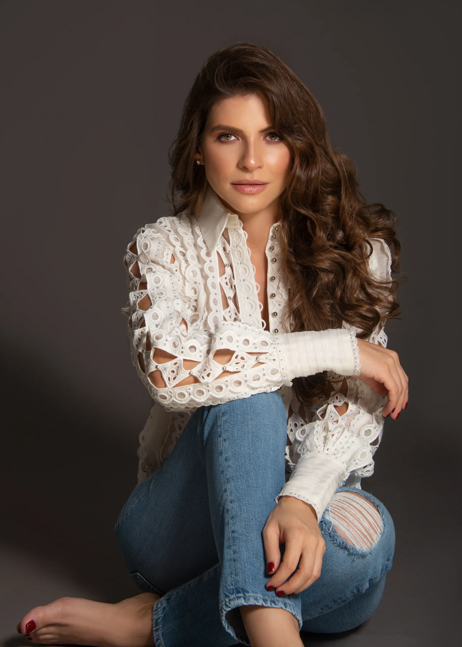 A woman sitting on the ground wearing jeans and a white shirt.